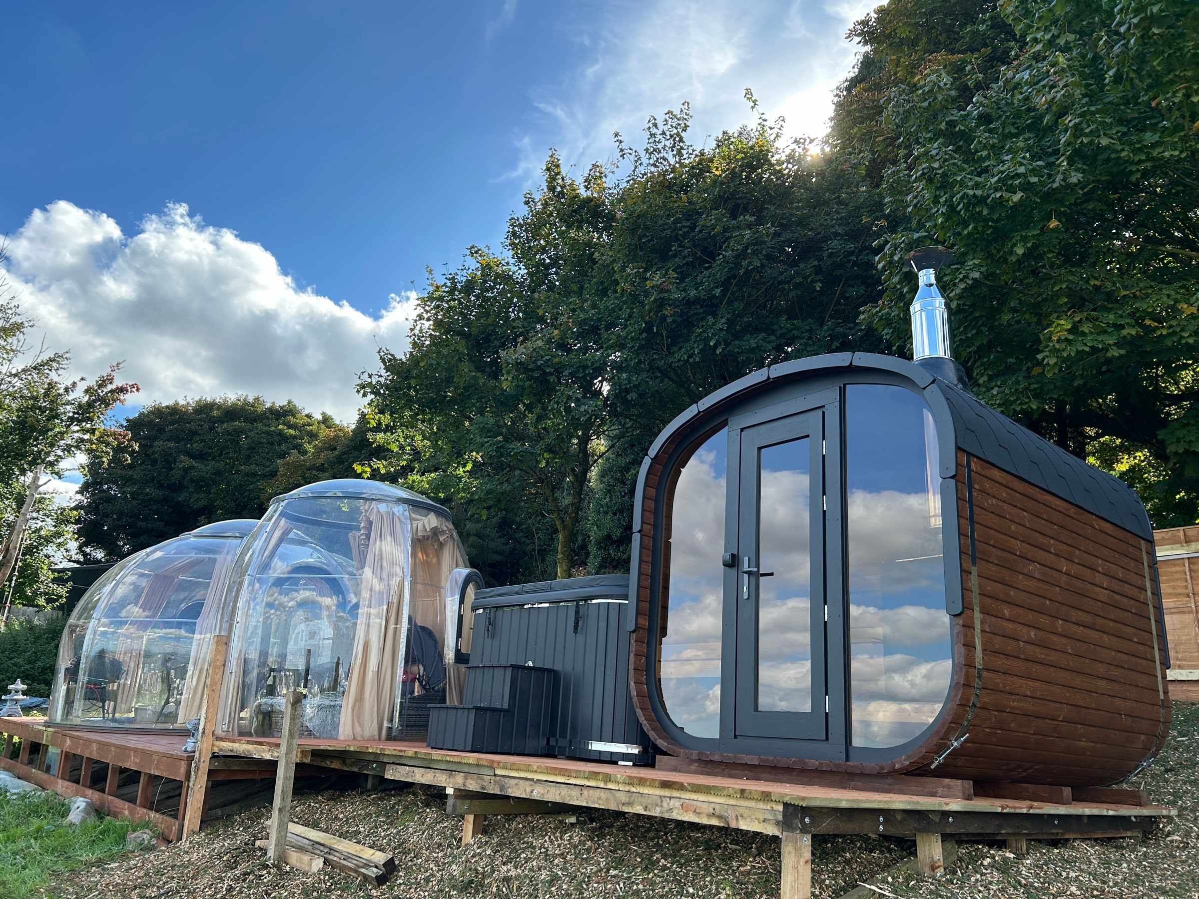 Woodland sauna and glass domes under a blue sky at Happy Land Farm
